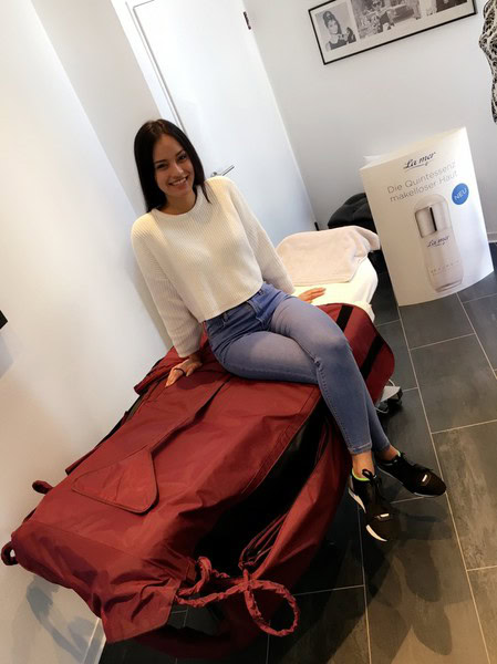 Frau sitzt auf roter Tasche im Kosmetikstudio.